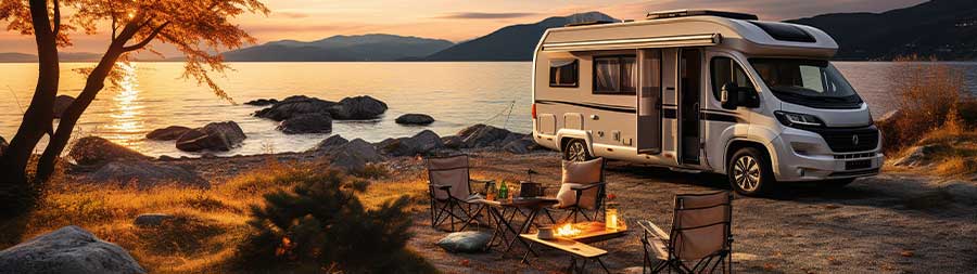 RV parked next to a camp fire by the lake at sunset.