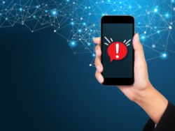 A woman holds up her cellphone. An exclamation mark is on the screen.