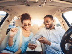 A couple sit inside their car and look at a cellphone.