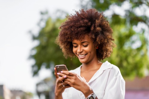 A lady smiles while she uses her cellphone to text.