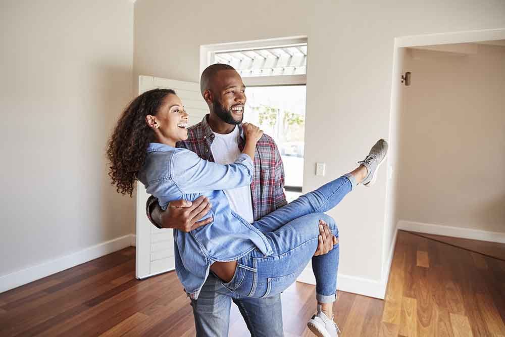 A man carries a woman into a new home as they smile.