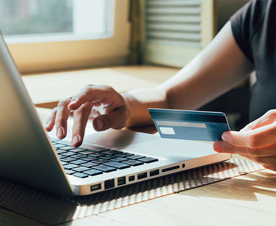 Hand holding a Credit Card next to a Laptop.