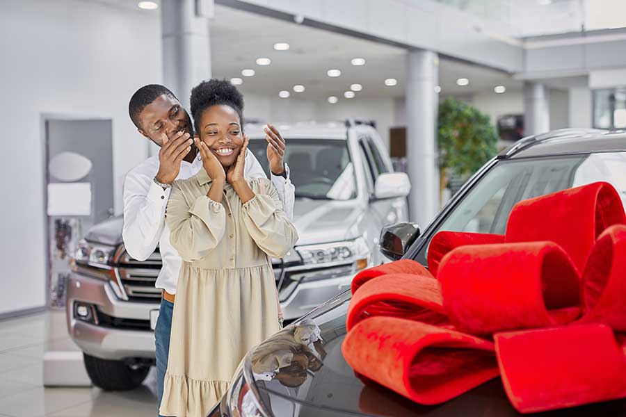 A man surprises a woman with a car with a bow on it.