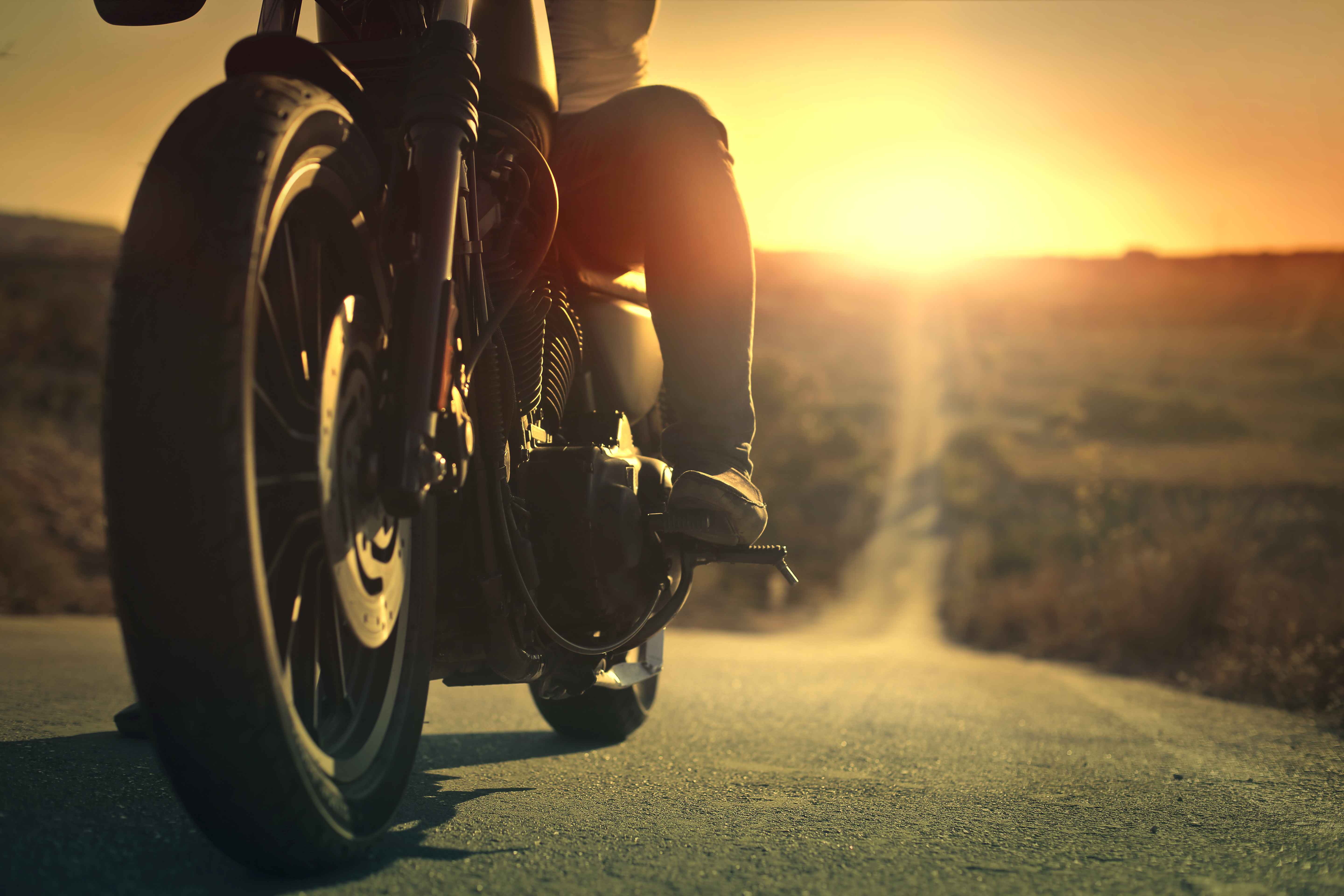 A man sits on a motorcycle on a road during sunset.