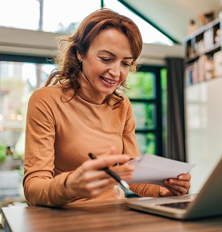 Woman looking at papers in front of laptop at home.