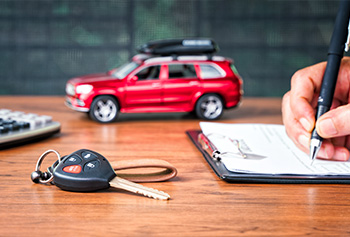 Small red car on a desk next to someone signing papers.