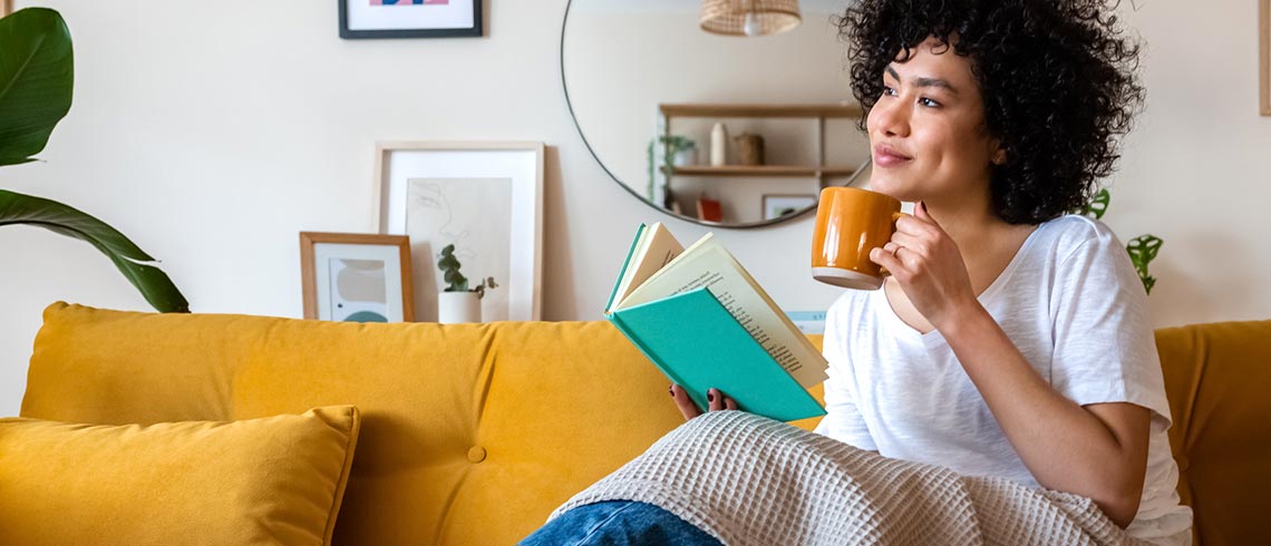 Woman sipping coffee and reading a book at home.