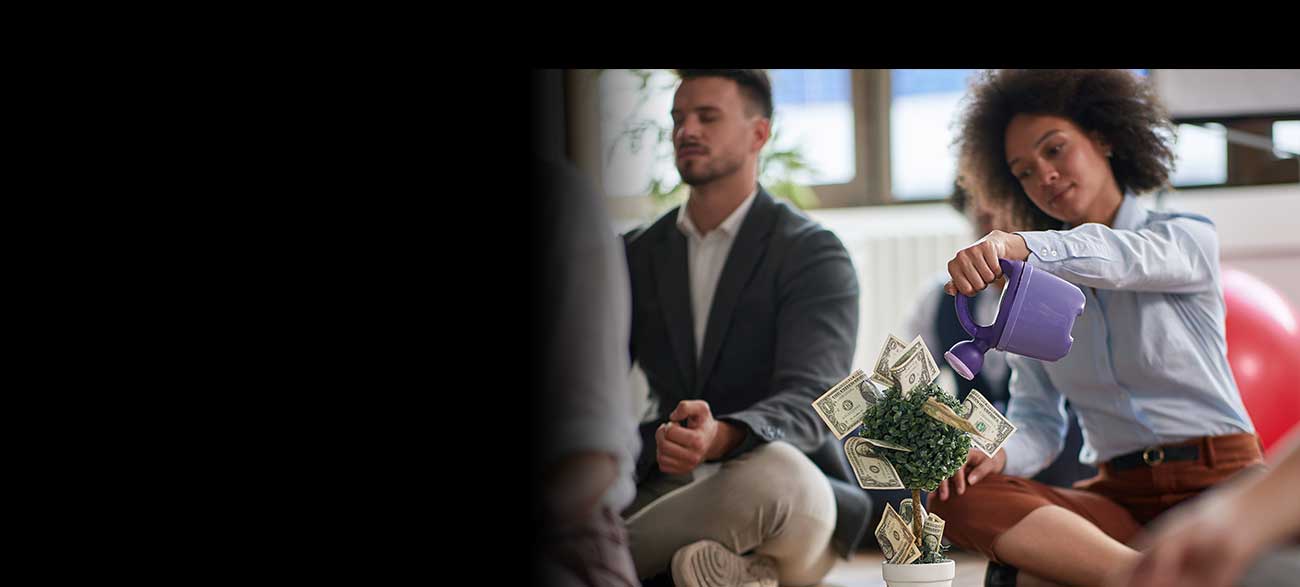 A lady pour water on a little tree with dollars sticking out of it.