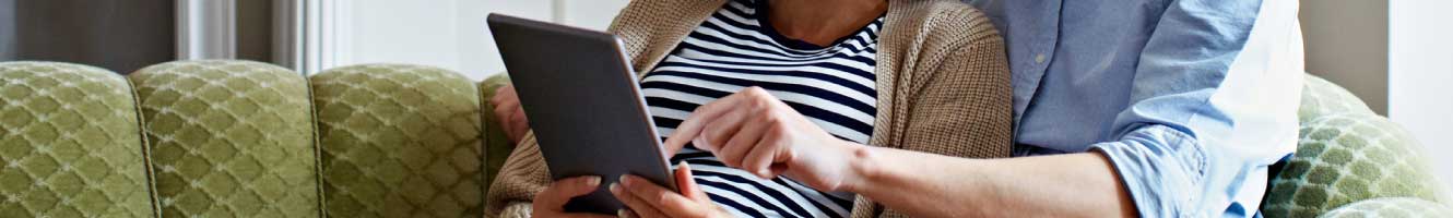 A couple uses a tablet siting on the couch.