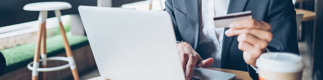 A man holding his debit card while typing on his laptop.