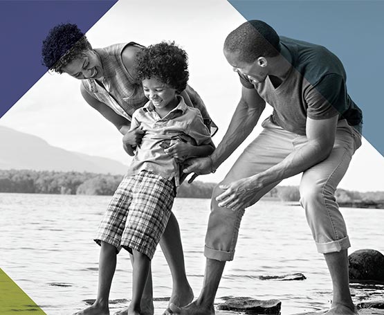 Parents and child playing near the water.