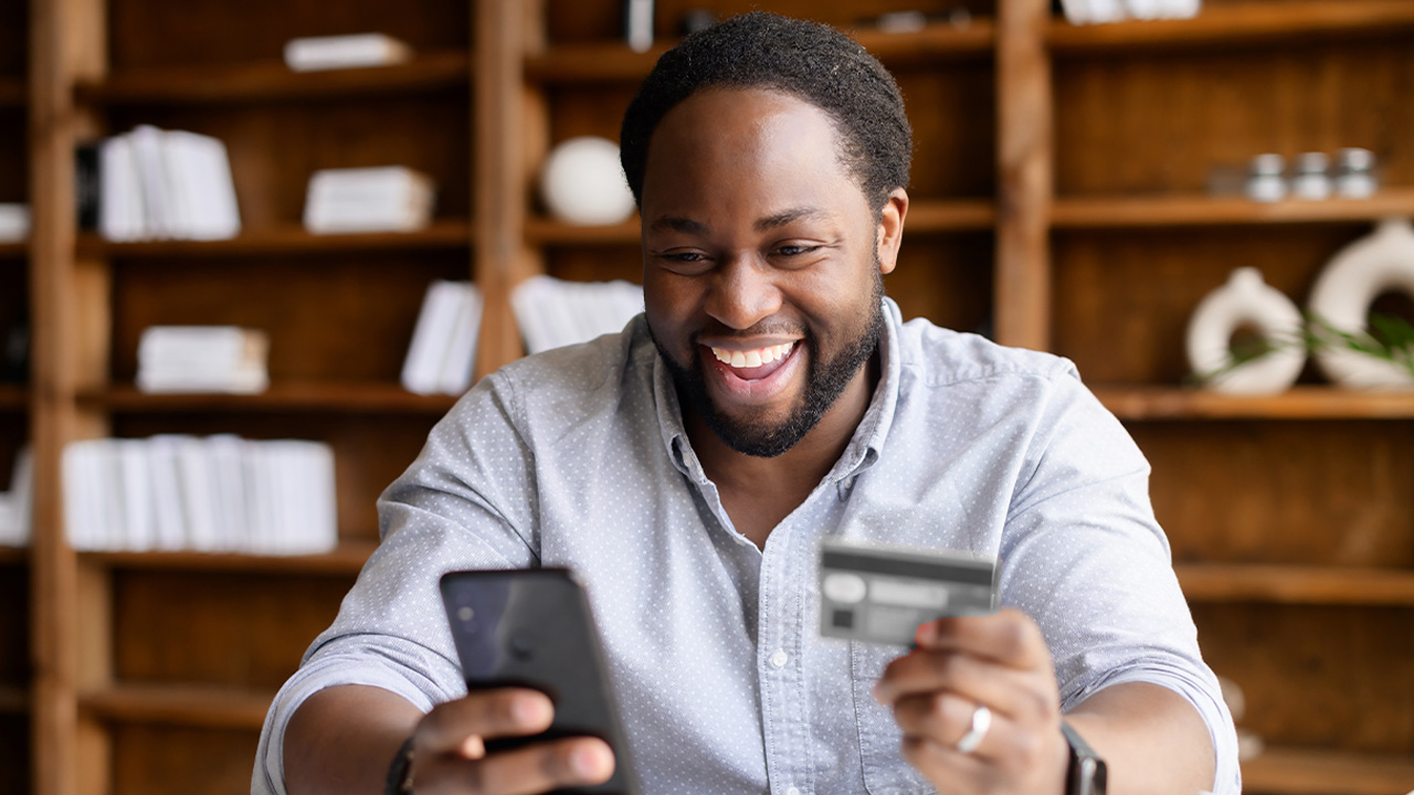 A man laughs while holding a credit card.