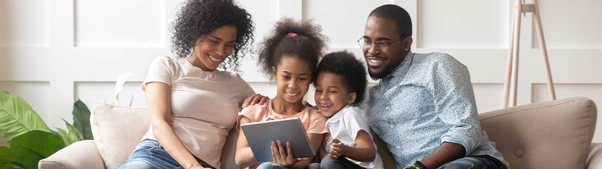 African American family sitting on the couch looking at an iPad and smiling. 