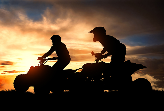 2 men on ATVs during sunset.